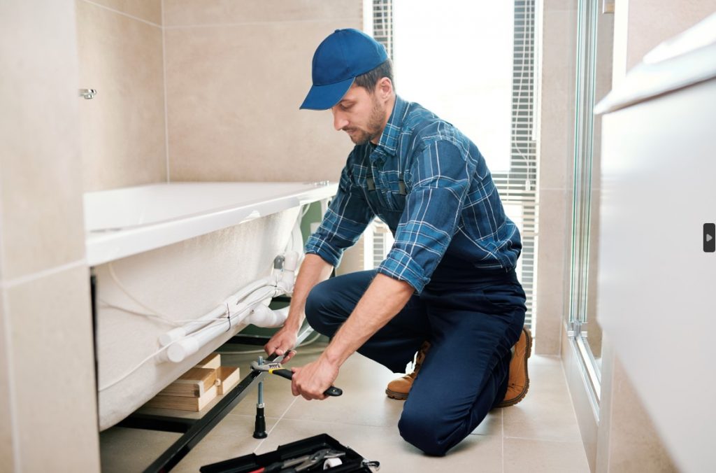 Young plumber working on a bath | Featured image for How to Unblock a Bath Drain – Our Top 5 Ideas blog by Akins Plumbing.