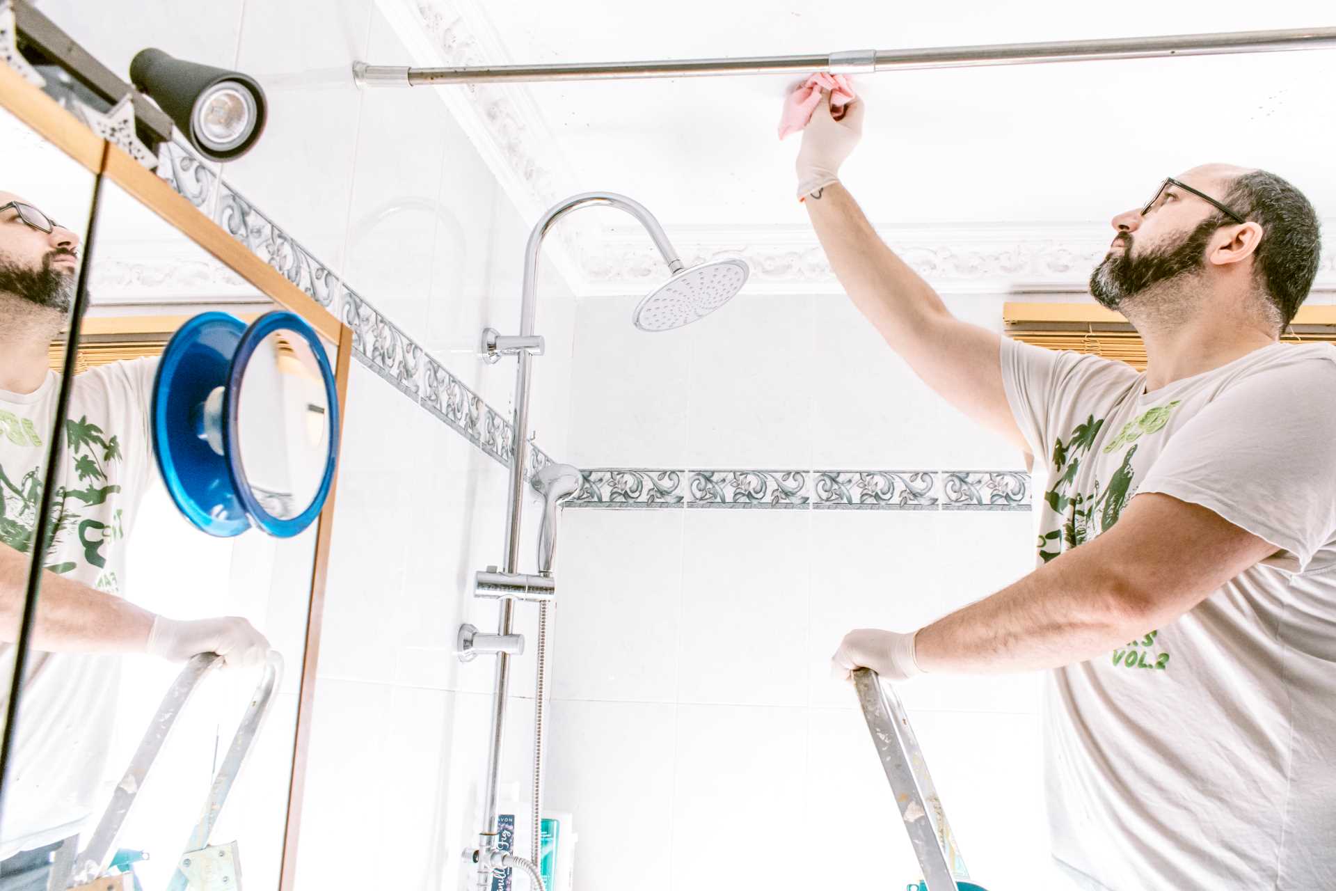 Man cleaning mould off a bathroom ceiling | Featured image for Our Guide on How to Prevent Mould in Bathrooms blog by Akins Plumbing.