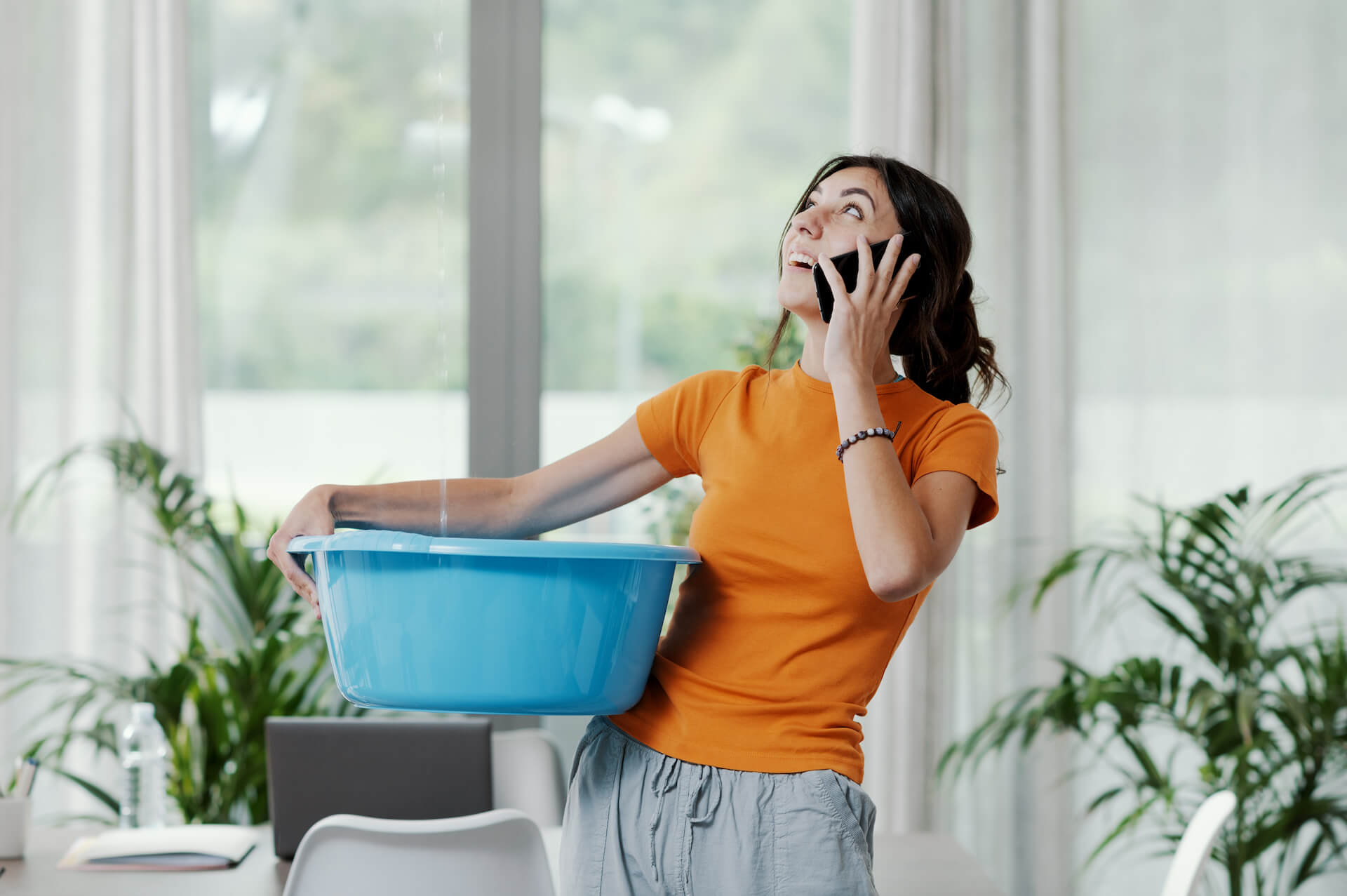Woman calling for water leak repair while collecting water leaking from the ceiling in a bucket | Featured image for the Plumbing Repair Services Page from Akins Plumbing.